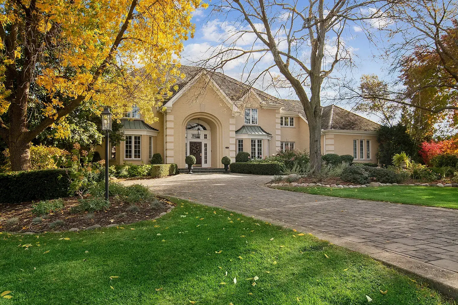 Stone driveway curving through autumn trees to the cream stucco front of the house