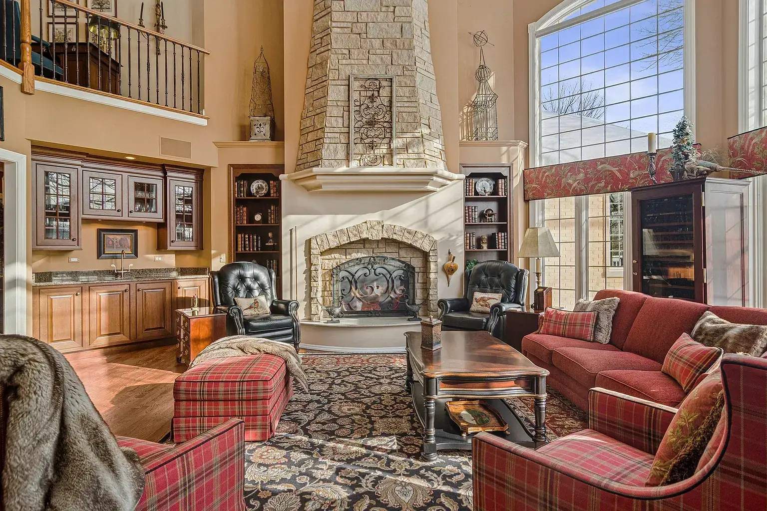 Great room with a stone fireplace, tall windows and a balcony above