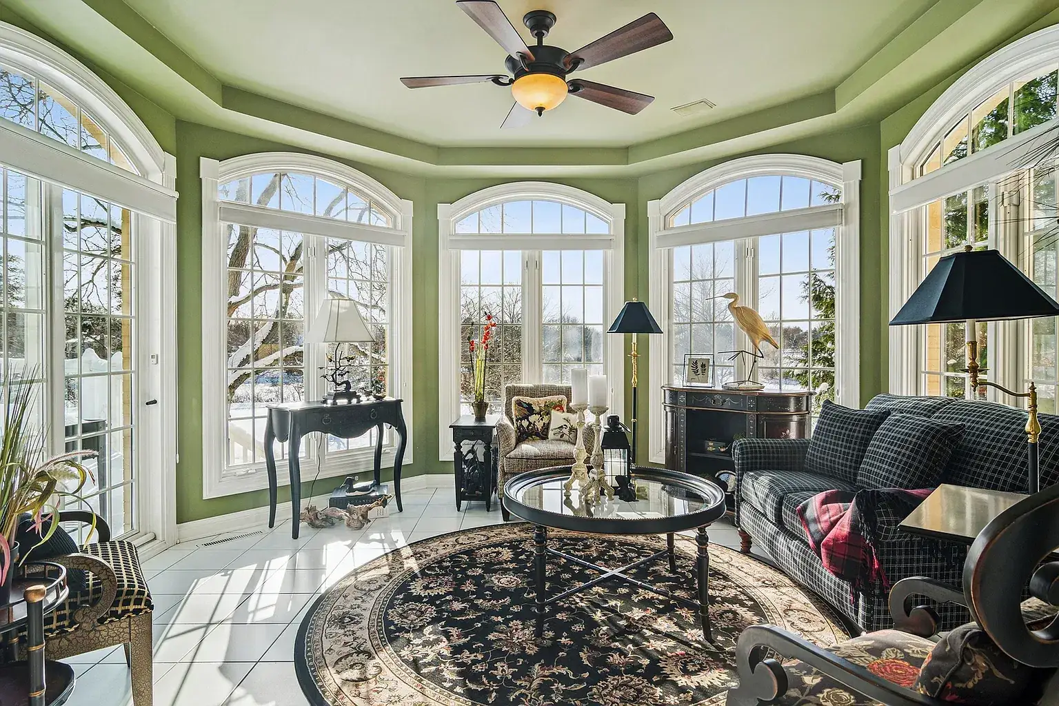 Sun room ringed with tall arched windows, green walls and a ceiling fan
