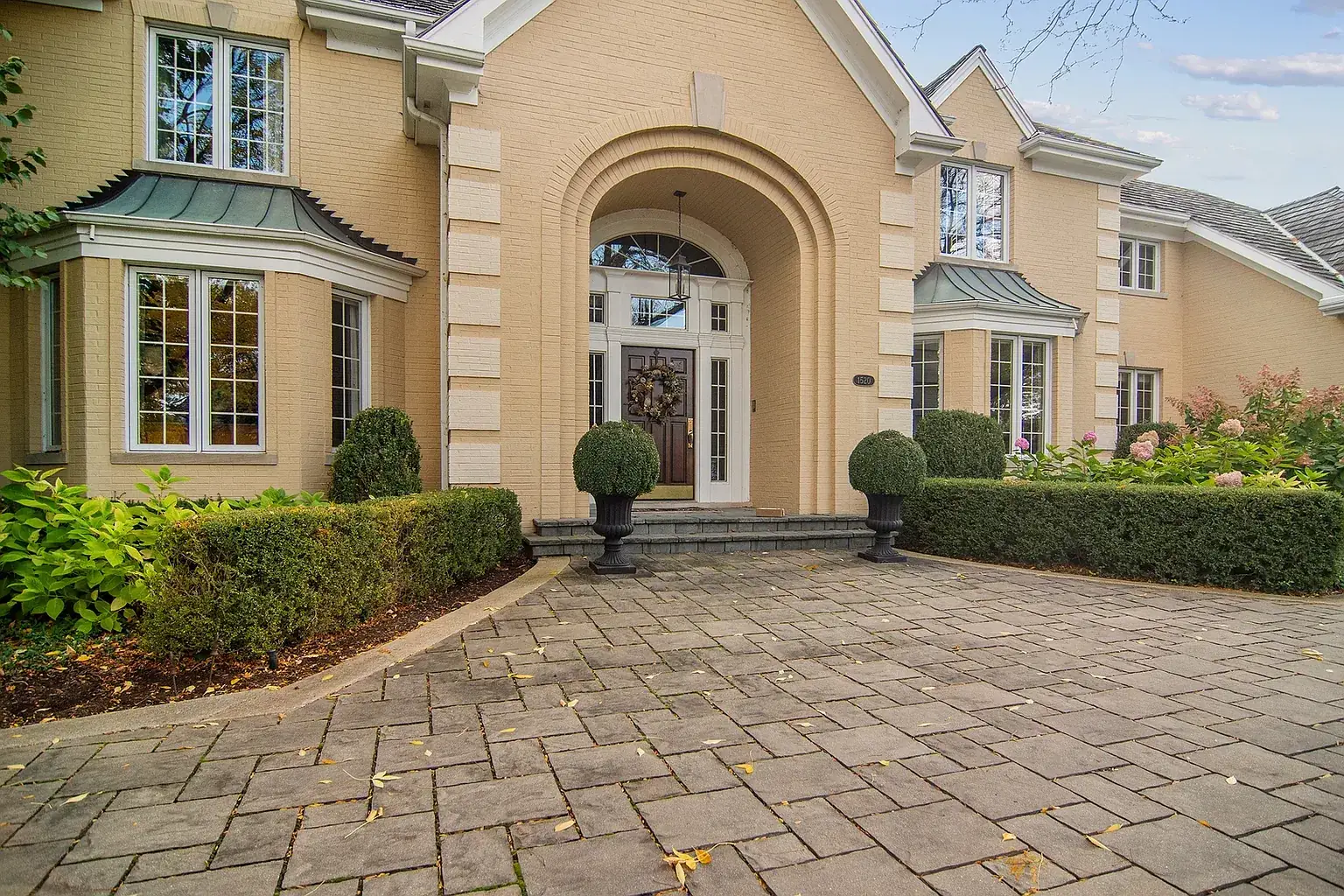 Arched front entry above a stone courtyard, with boxwood in urns
