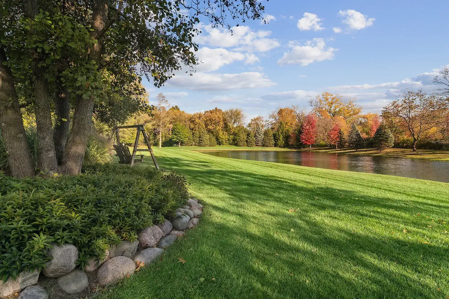 Lawn sloping down to a pond lined with autumn trees